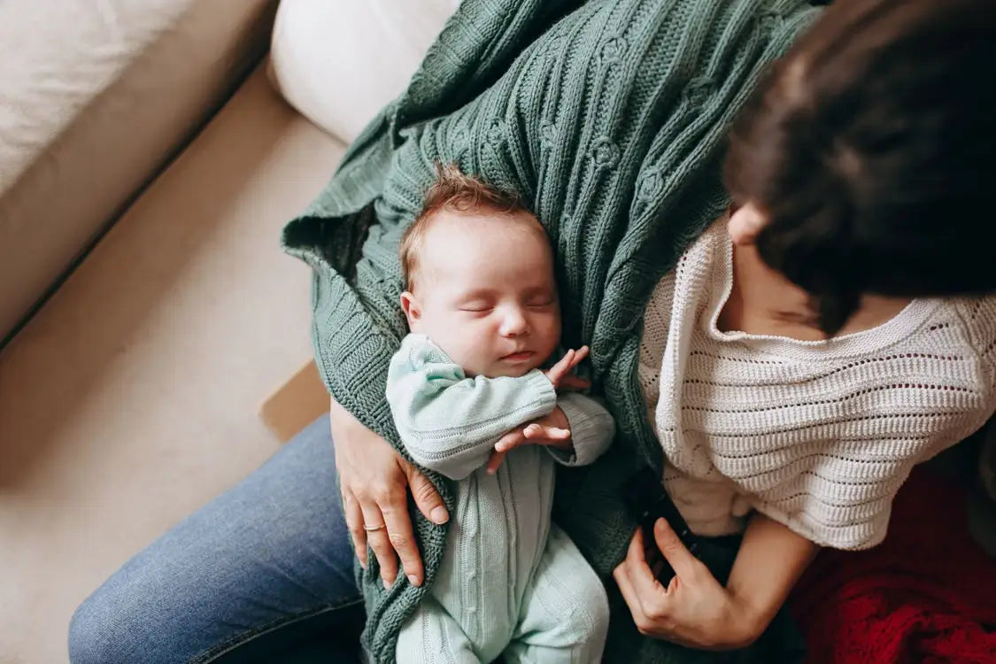Mother holding a sleeping newborn baby wrapped in soft knitted clothing at home