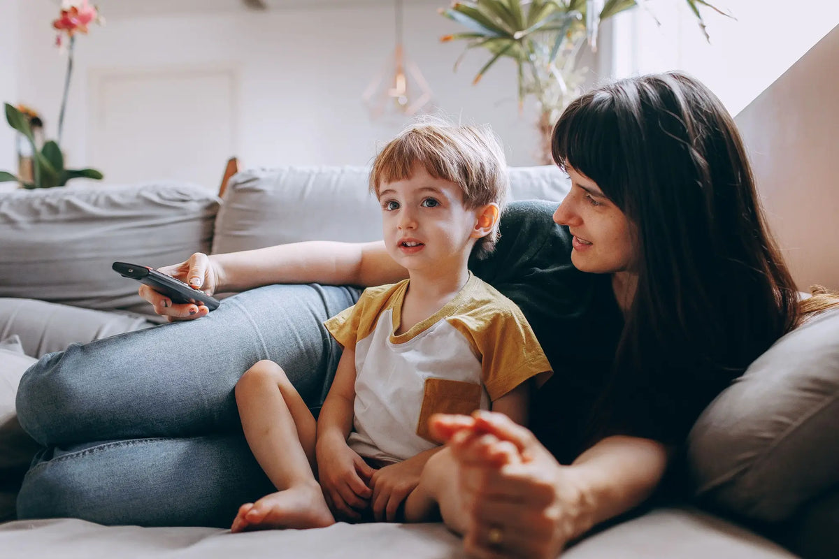 A mother and young child sitting together on a sofa and watching television at home.