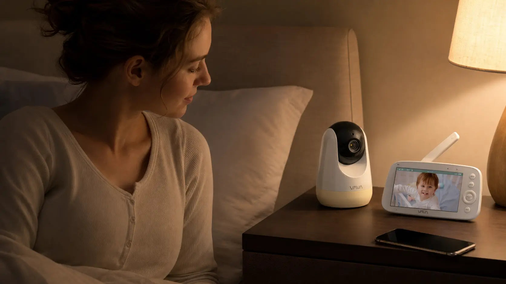 Mother checking a smart baby monitor camera with night vision and video display beside the bed, providing real-time monitoring of her baby during the night