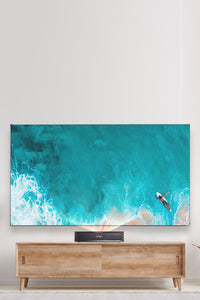 VAVA Chroma Triple Laser 4k Projector on a wood TV Stand with a blue beach on the large screen