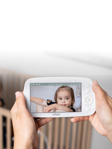 Caregiver holding VAVA baby monitor with baby in a crib in the background