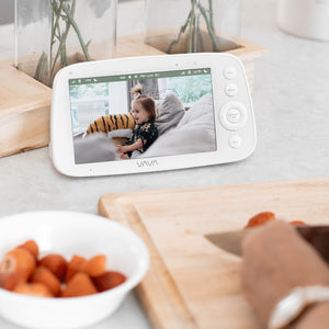 VAVA baby monitor resting on a counter with a bowl of fruit and cutting board
