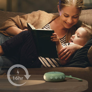 VAVA Twinkle Soother nightlight on a table while a mother and child look at a book in the background.