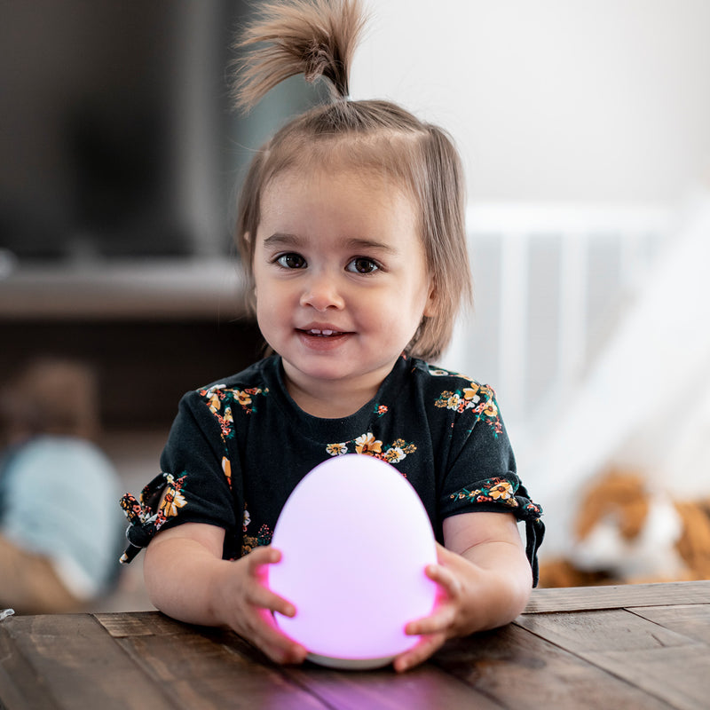 Toddler girl sitting a wood table holding a pink VAVA baby night light