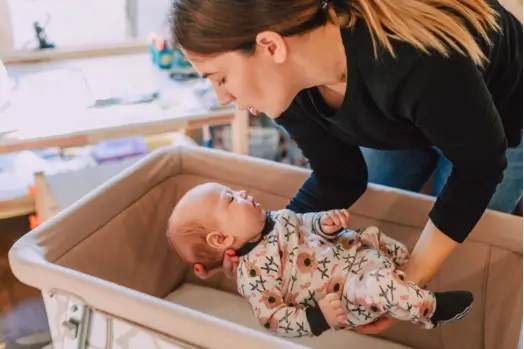 Mother gently lifting and caring for her baby in a crib at home