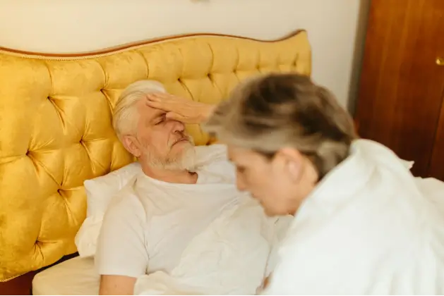 Older man resting in bed with his hand on his forehead while feeling unwell