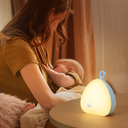 A mother gently feeding her baby while a VAVA Peep-a-Light night light and soother rest on the nearby table.
