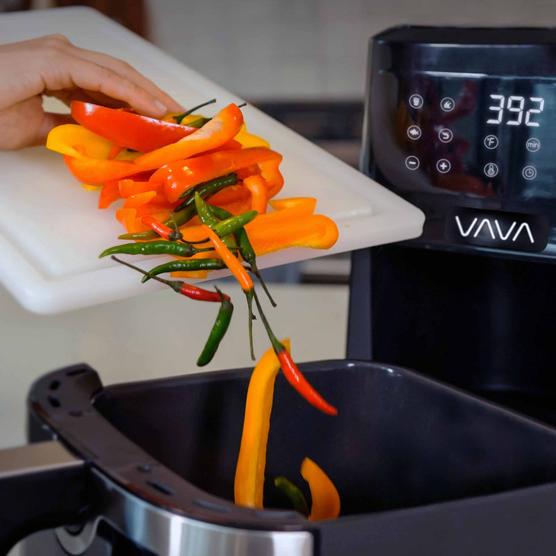 A person is putting colorful peppers into the VAVA air fryer basket.