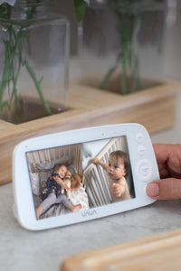 Caregiver holding a VAVA split screen baby monitor on a kitchen counter with bowl of tomatoes in background