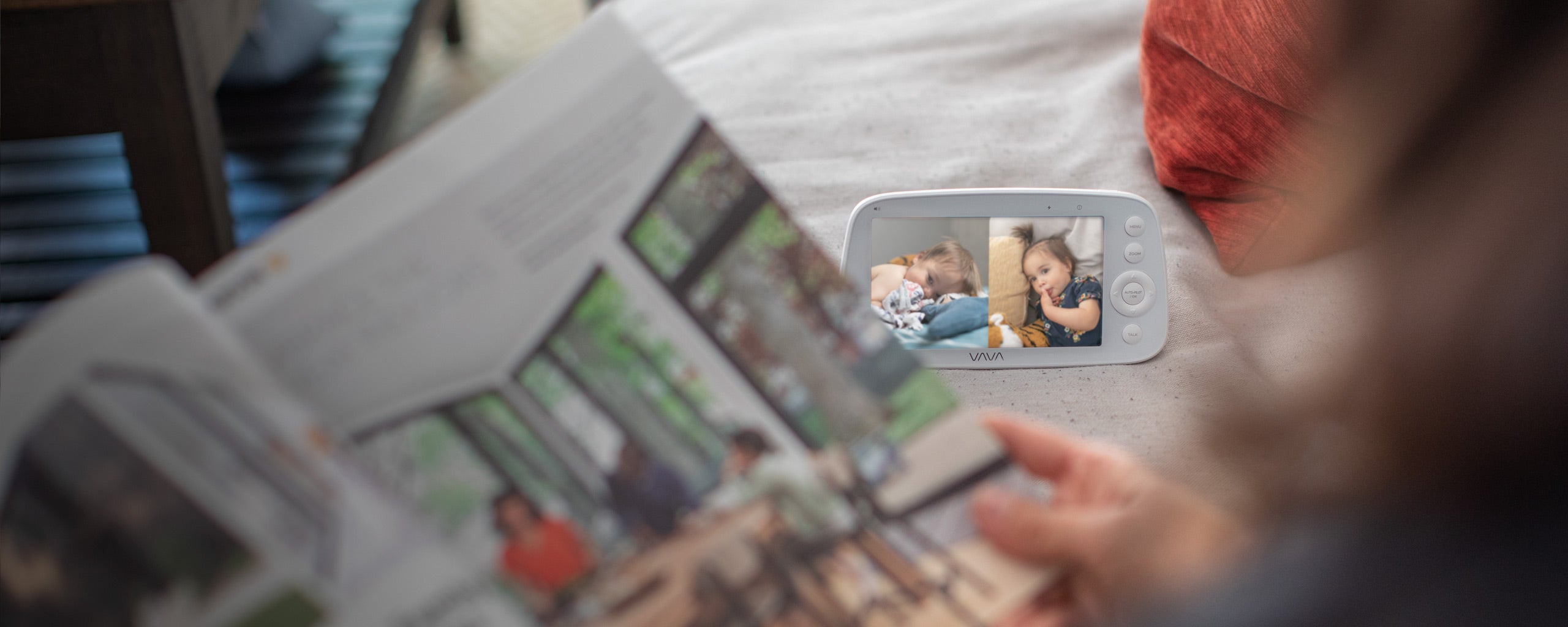 VAVA split screen baby monitor in background, caregiver looking at a book in the foreground