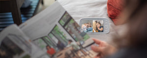 VAVA split screen baby monitor in background, caregiver looking at a book in the foreground