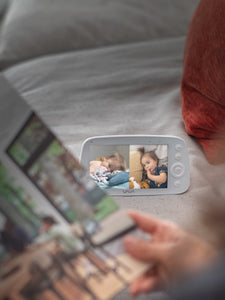 VAVA split screen baby monitor in background, caregiver looking at a book in the foreground