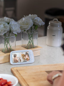 VAVA split screen baby monitor resting on a counter with bowl of tomatoes and brown cutting board in foreground