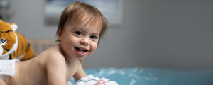 Smiling baby in a diaper with a stuffed tiger in the background