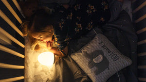 Toddler laying in a crib with a VAVA night light and pillow