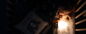 Toddler girl laying in a crib with a yellow VAVA baby night light