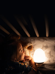 Toddler girl laying in a crib with a yellow VAVA baby night light