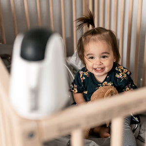 Child in a crib looking at a VAVA baby monitor camera in the foreground