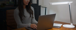 Woman working on her laptop with a white VAVA desk lamp next to her