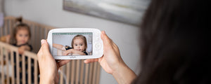 Caregiver holding VAVA baby monitor with baby in a crib in the background