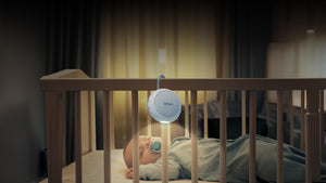 VAVA Twinkle Soother night light hanging from a crib, baby sleeping in the crib in a nursery.