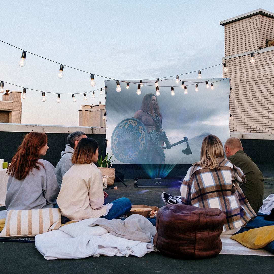 5 people sitting around the VAVA Chroma triple laser projector and screen in an outdoor movie setting