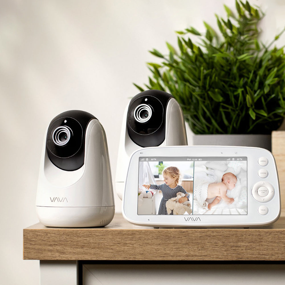 VAVA split screen baby monitor displaying a toddler and sleeping baby, 2 camera, and a green plant in the background