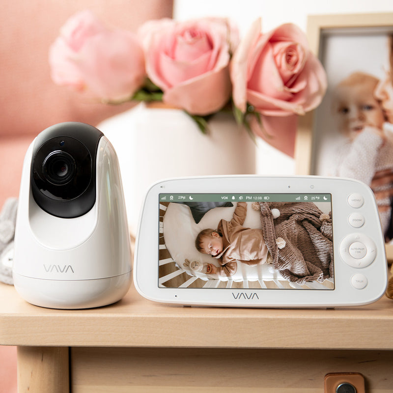 VAVA baby monitor and camera on a table with pink flowers and a picture frame