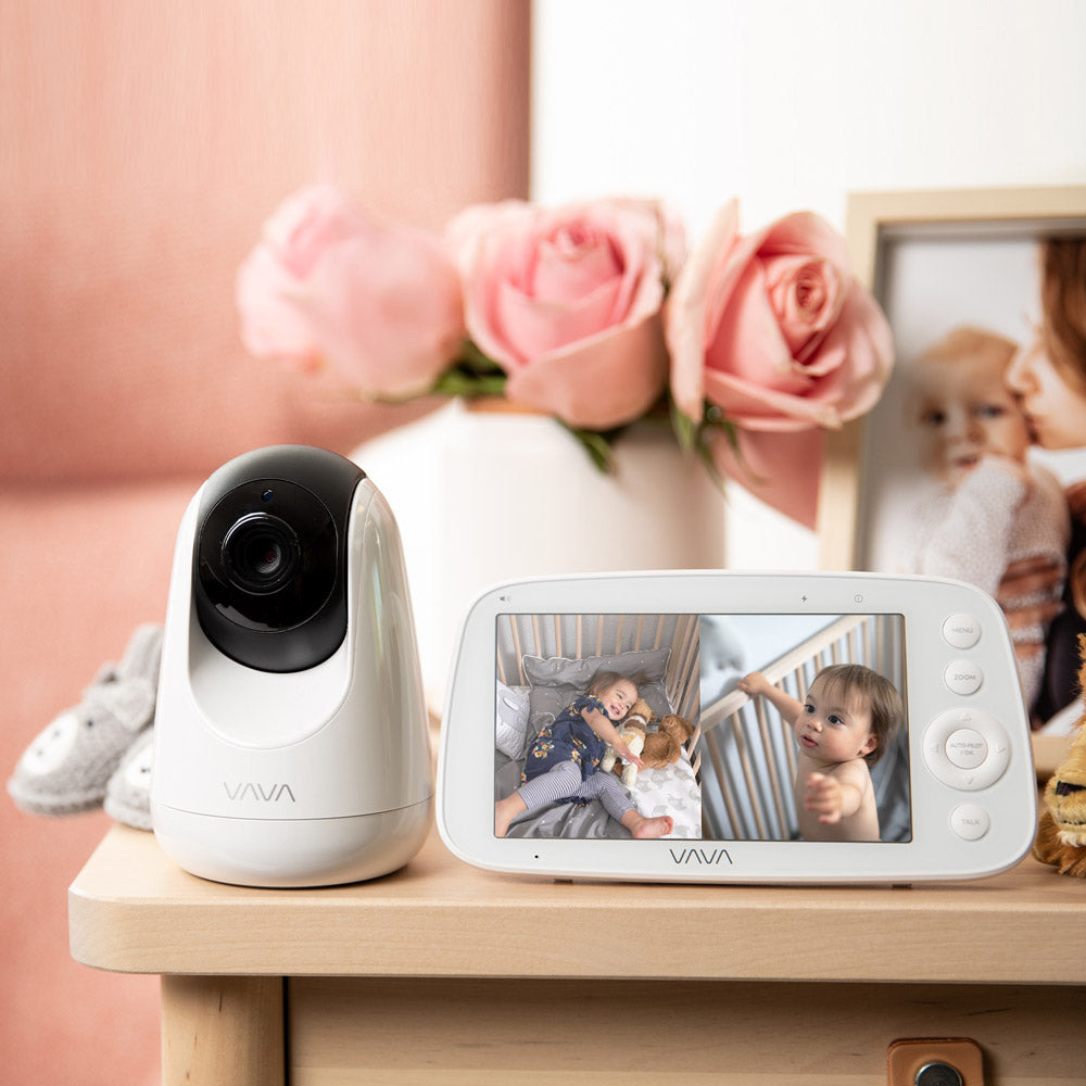 VAVA split screen baby monitor and camera on a table with pink flowers and a picture frame in background