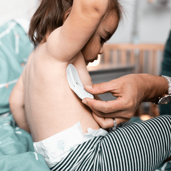 Caregiver placing VAVA smart thermometer in VAVA adhesive on a child’s side